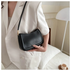 Chic black minimalist shoulder bag with gold buckles worn over a white blazer