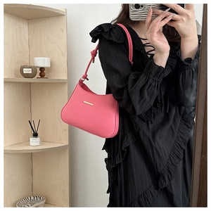 Dettaglio borsa sottobraccio rosa con barra in metallo dorato e cinturino decorativo a nodo