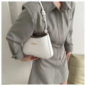 Close-up of minimalist white shoulder bag with knotted strap and gold metal hardware