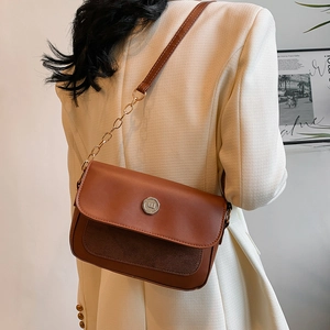 Detail view of brown patchwork leather shoulder bag with metal buckle on beige blazer