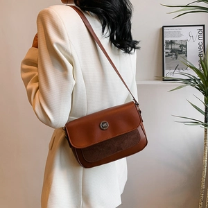 Brown leather crossbody bag with suede detail worn over a white blazer by a model