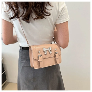 Close-up of light pink crossbody bag featuring a silver bow and decorative buckles