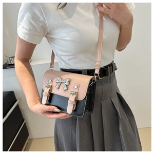Detail of crossbody bag with silver bow accent and contrasting flap on shoulder