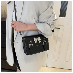 Detail of black bow crossbody bag with silver buckle straps and sleek leather texture