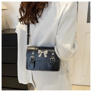 Detailed view of a black leather crossbody bag with a metallic bow on a white suit