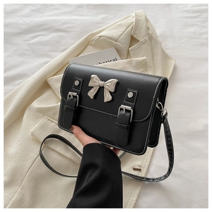 Detail of black crossbody bag featuring silver bow hardware and white contrast stitching