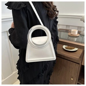 Close-up of a white structured handbag with a round handle, worn by a model in a cafe