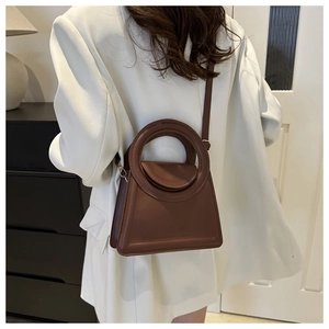 Brown faux leather crossbody bag with round handle worn over a white suit by a model