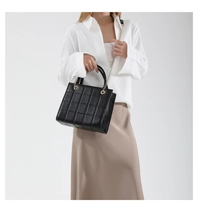 Detail of a quilted black crossbody bag with gold chain strap on a white shirt model