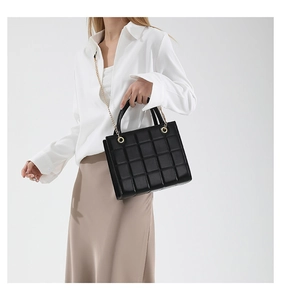 Close-up of black quilted shoulder bag featuring gold chain strap and metal round clasp