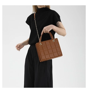 Detail of a brown quilted square handbag featuring a golden chain strap and leather handle