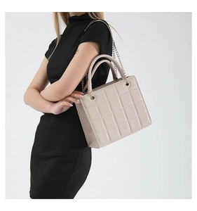 Detail of beige quilted flap bag featuring gold chain strap and top handle on a model