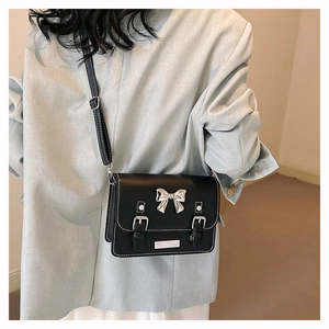 Detail of black crossbody bag with silver bow accent and white decorative stitching