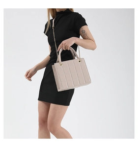 Detail of beige quilted leather mini bag with gold chain strap on black dress