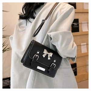 Close-up of black crossbody bag featuring a silver bow accent and white stitching details
