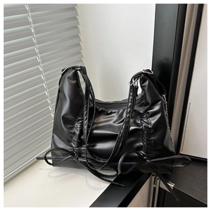 Detail of black pleated hobo bag with metal chain accents and side bow ties design