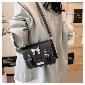 Detail of black leather crossbody bag with silver bow accent and white contrast stitching