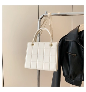 Detail of white quilted crossbody bag with gold chain strap and rigid top handle