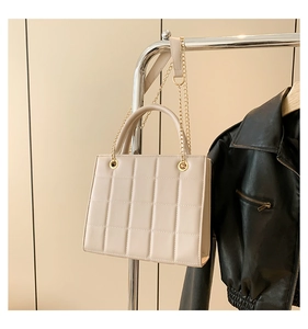Detail of beige quilted tote bag featuring golden chain strap and leather texture