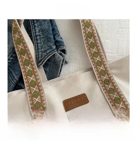 Gros plan du sac cabas en toile beige avec anses brodées et étiquette en cuir