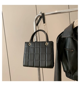 Detail of black quilted leather handbag with gold chain strap and metal handle