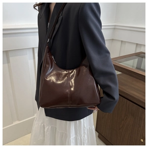 Close-up of a brown retro hobo bag in glossy faux leather on a model's shoulder