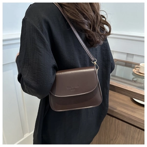 Detailed back view of a dark brown leather crossbody bag worn by a model in soft light