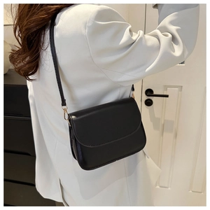 Detail of a black faux leather rectangular crossbody bag styled with a white blazer