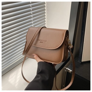 Detail of brown faux leather crossbody bag with embossed logo and golden metal buckle