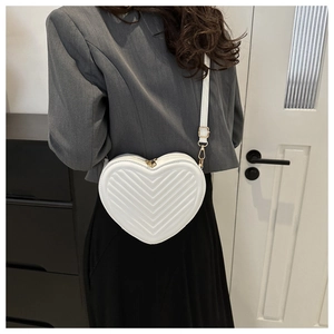 Macro shot of white heart-shaped crossbody bag featuring V-shaped quilted texture and gold zip