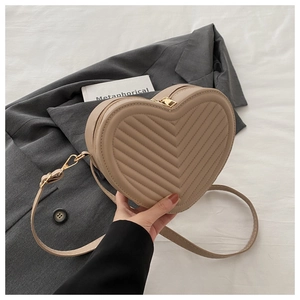Detail of a beige V-quilted heart-shaped crossbody bag with elegant gold hardware zipper