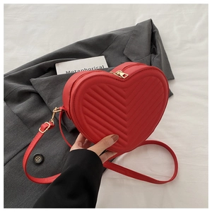 Detail of red heart-shaped leather crossbody bag with V-quilted texture and gold zipper