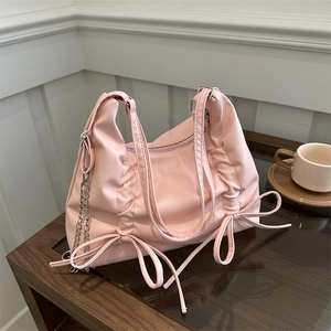 Pink soft faux leather shoulder bag with decorative bows and silver chain on wood