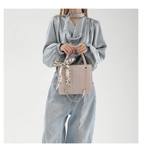 Detail einer beigen gesteppten Handtasche mit gemustertem Seidentuch und Metallkette