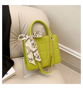 Detail einer grünen Stepptasche mit dekorativem Seidenschal und goldenem Kettenriemen