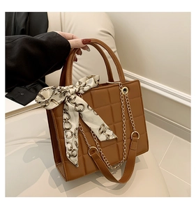 Detail einer braunen Stepphandtasche mit einem Seidentuch am Griff und goldener Kettenriemen