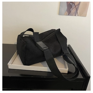 Detail view of black corduroy messenger bag on white tray with adjustable strap