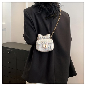 Mini white tweed crossbody bag with bow detail and gold chain strap shown on a person