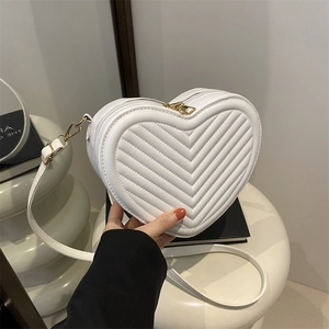 White heart-shaped crossbody bag with V-quilting and gold zipper on artistic table