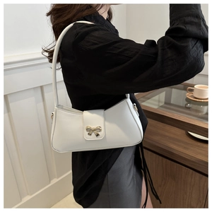 Detail of white crescent underarm bag with gold bow clasp on a model in a minimal setting