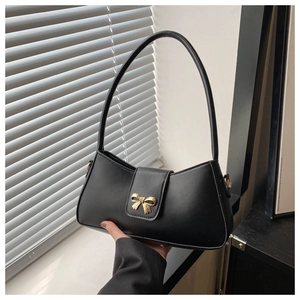 Close-up of black crescent shoulder bag featuring a gold bow-shaped metal clasp