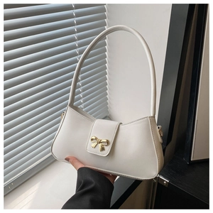 Detail of white PU leather crescent bag with golden bow buckle and soft natural light