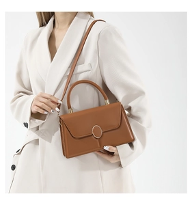 Detail of caramel leather crossbody bag with silver oval metal buckle on a model
