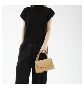 Detail view of light brown minimalist leather handbag with oval buckle and textured finish