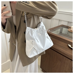 Close-up of white drawstring bucket bag featuring silk bows and silver chain straps