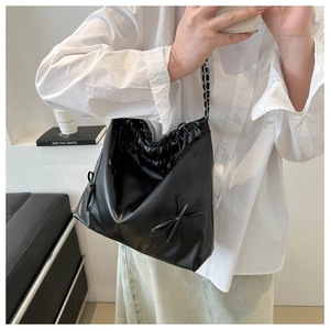 Close-up of black PU leather underarm bag with drawstring and double bow detail