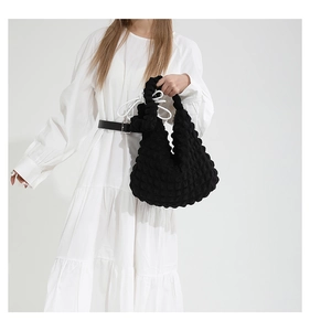 Detail shot of black popcorn texture shoulder bag on model with white dress