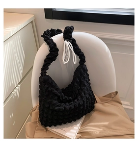 Detail of black pleated cloud tote bag featuring 3D puff texture on a modern chair