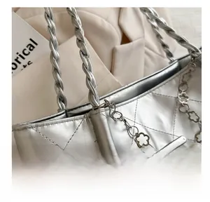 Close-up of silver quilted tote bag with woven handle and pearl charm detail