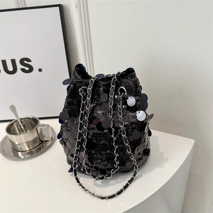 Chic black sequin bucket bag with silver chain strap on a modern minimalist desk